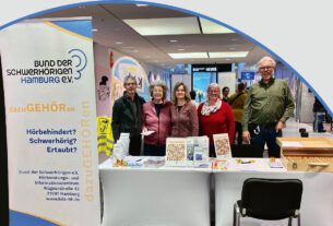 Titelseite der Zeitschrift „BdS aktuell“, Heft 3, Mai und Juni 2026. Fünf Personen stehen hinter einem Informationsstand des Bundes der Schwerhörigen Hamburg in der Hamburger Meile. Auf dem Stand liegen Informationsmaterialien und Angebote rund um Hörbehinderung und Kommunikation.